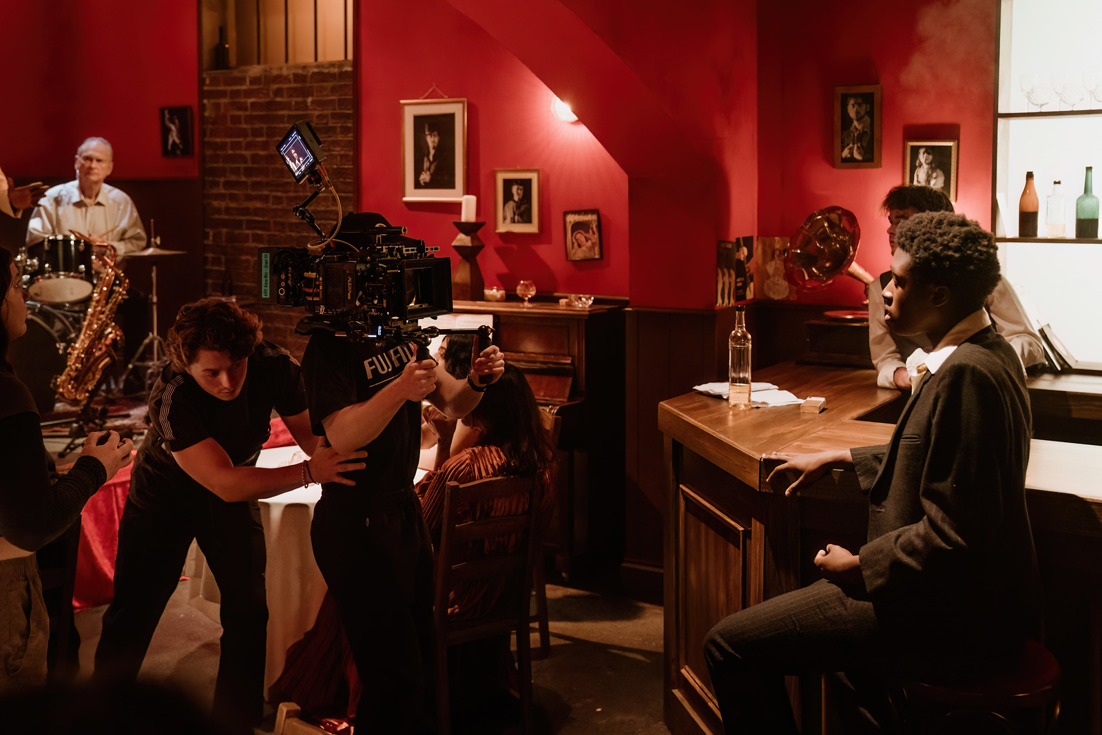 Behind the scenes still of "All My Blues", showing the director guiding a camera operator on set, while an actor sits at the edge of a bar.