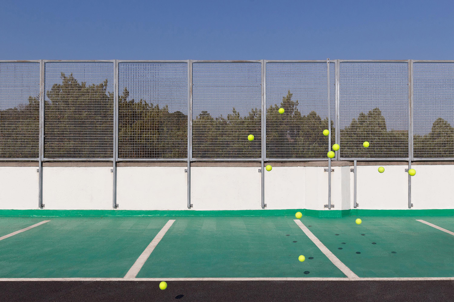 Tennis balls suspended in a car park with green parking spaces and metal borders, resembling a tennis court.