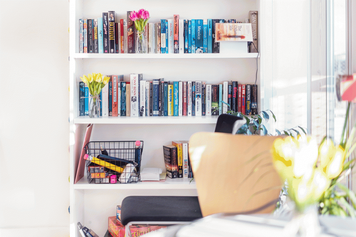 Image of a book shelf with two full rows of books and a basket of stationary.